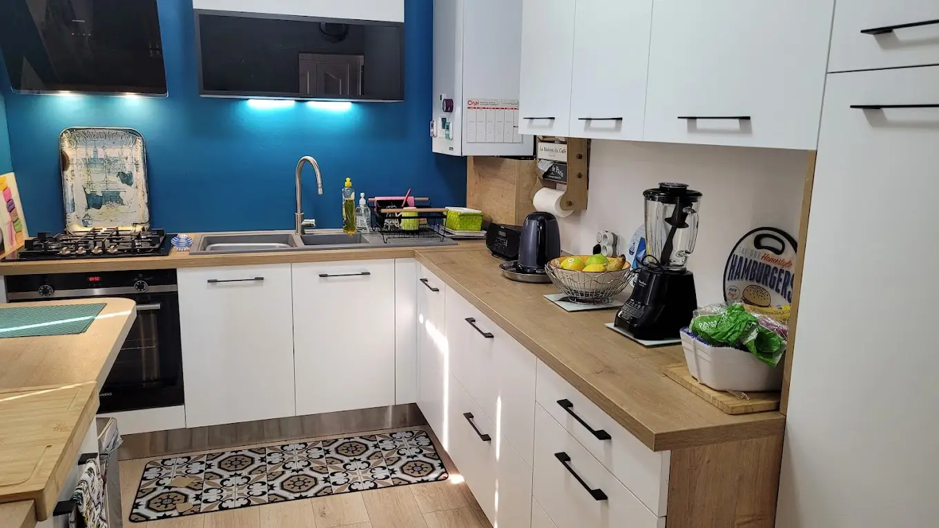 Cuisine blanche avec plan de travail bois et mur d'accent bleu pétrole