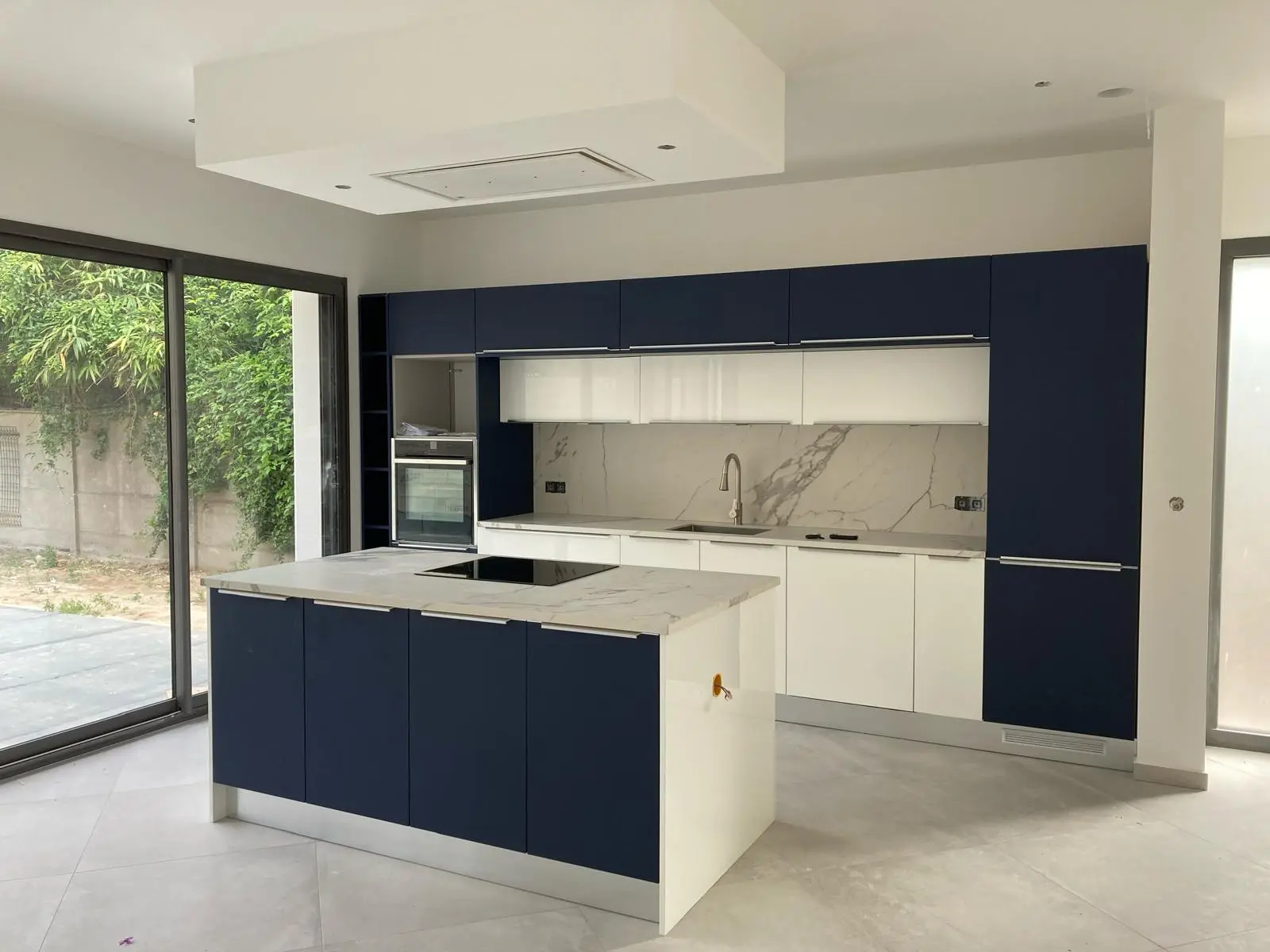 Cuisine bleu nuit et blanc avec îlot central en marbre, ouverte sur le jardin